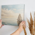 A peaceful painting of a sailboat sailing on calm ocean waters with clouds in the sky