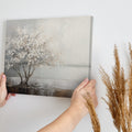Textured painting of a tree with white flowers and its reflection on water, on a beige and brown background