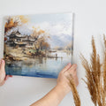 Canvas art of a tranquil oriental landscape with autumnal trees, traditional architecture, calm water, and mountains in the background.