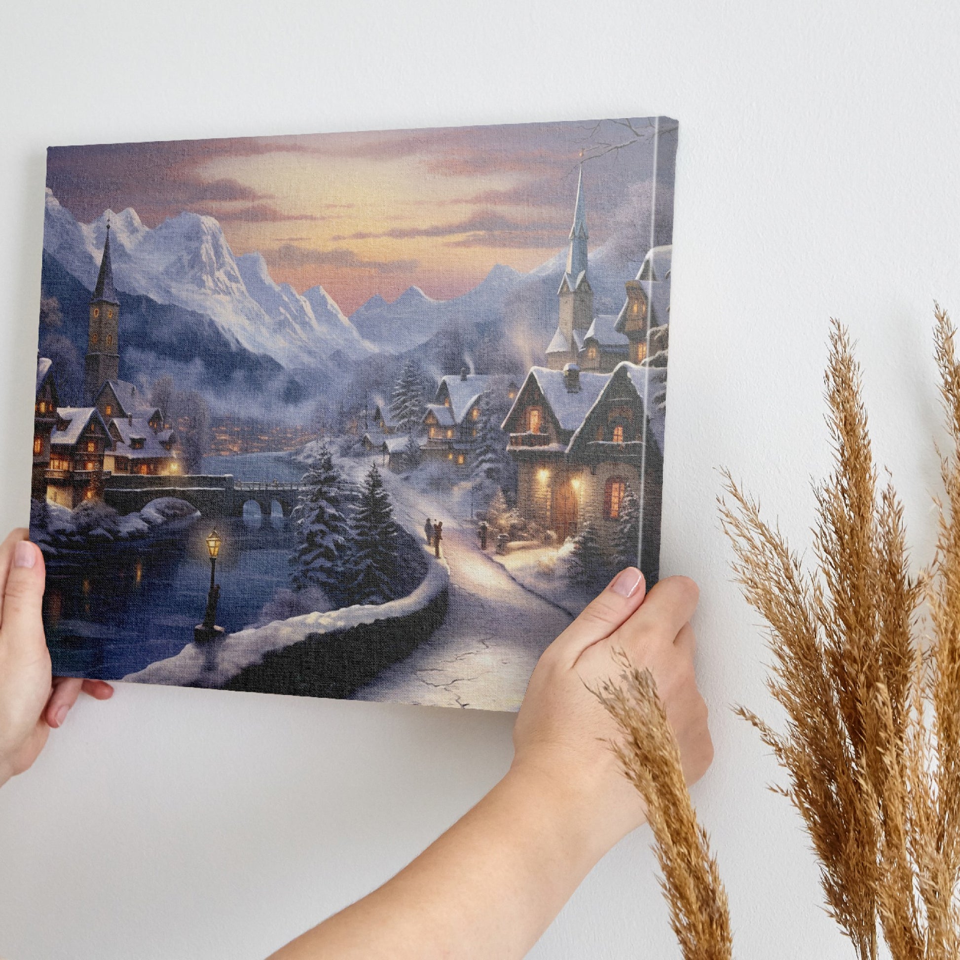 Framed canvas print of a snowy Alpine village at twilight with warm glowing cottages and snow-capped mountains