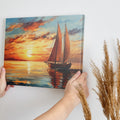 Impressionistic canvas painting of a sailboat at sunset with vivid orange sky and calm sea reflections