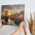 Framed canvas print of a historical port with sailing ships at sunset, featuring warm golden hues and reflective water