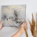 Framed canvas print of a snowy countryside scene with walking figures and a rustic cottage