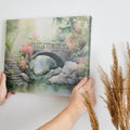 Framed canvas print of a serene stone bridge over a stream in a misty garden with lush greenery and flowering plants