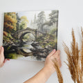 Framed canvas print of a tranquil autumnal scene featuring a rustic stone bridge over a serene river with lush forest in the background