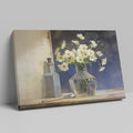 Framed canvas print of white flowers in glass vase with vintage bottle on a neutral background