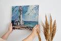 Framed canvas print of lighthouse on coastal rocks with dynamic sea and sky