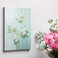 Framed canvas print of white blossoms with green leaves on a soft blue background