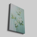 Framed canvas print of white blossoms with green leaves on a soft blue background