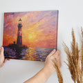 Impressionistic painting of a lighthouse at sunset with orange sky and blue sea