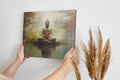 Framed canvas print of a serene Buddha in meditation with an abstract, earth-toned backdrop and reflective water