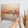 Framed canvas painting of a sailboat at sunset with orange and beige sky reflected in calm blue waters