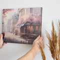 Framed canvas print of a Parisian cafe on a cobblestone street with cherry blossoms in full bloom