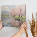 Framed canvas print of a tranquil river landscape featuring blooming cherry blossoms and a boat, in Impressionist style