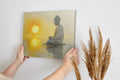 Framed canvas print of a meditative figure with the sun setting over water, reflecting golden tones