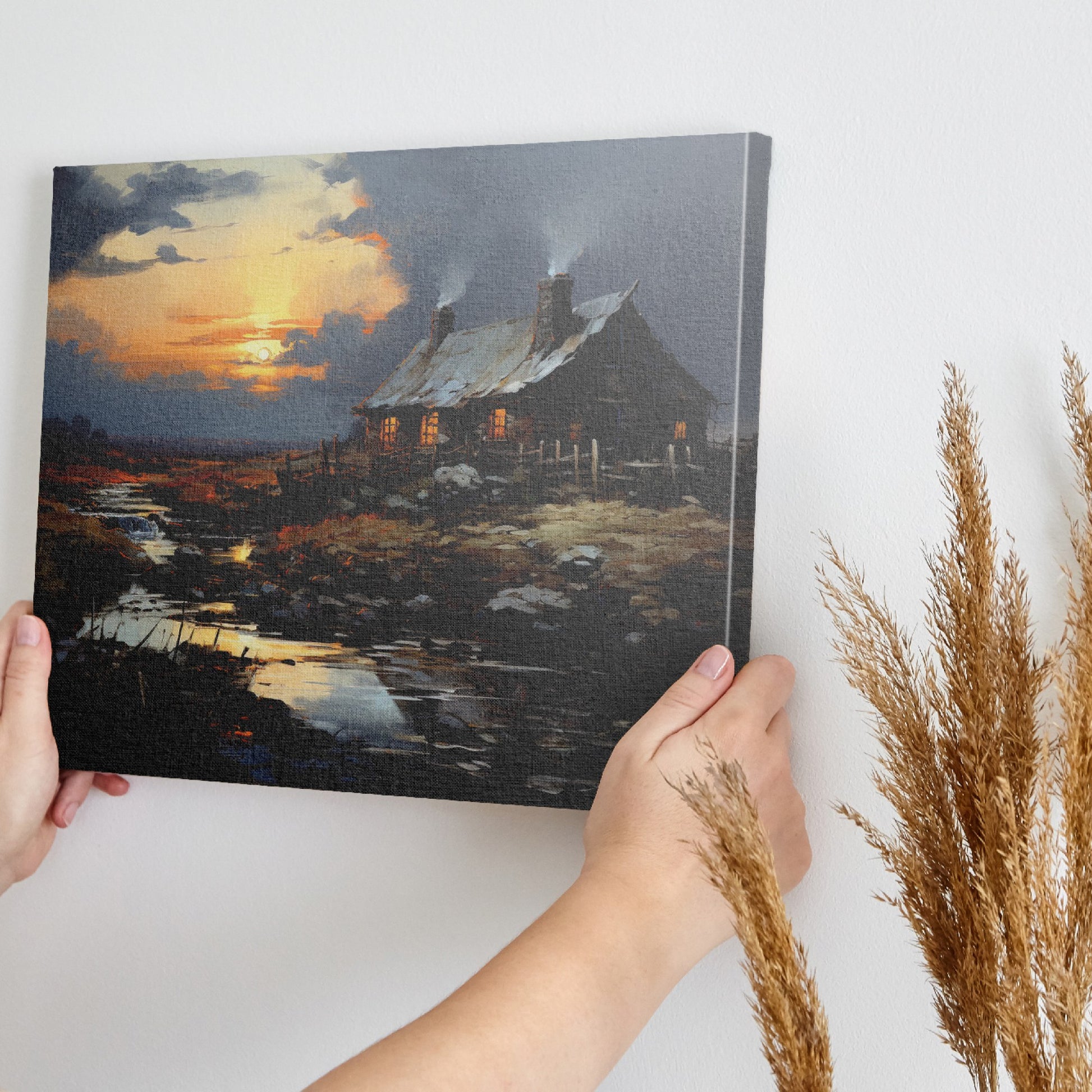 Framed canvas print of a rustic cottage with illuminated windows at sunset, set against a serene countryside landscape with a reflective creek.