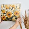 Framed canvas print of golden sunflowers and green foliage on a neutral background