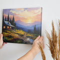 Framed canvas print of a rustic cabin at sunset with a mountainous backdrop